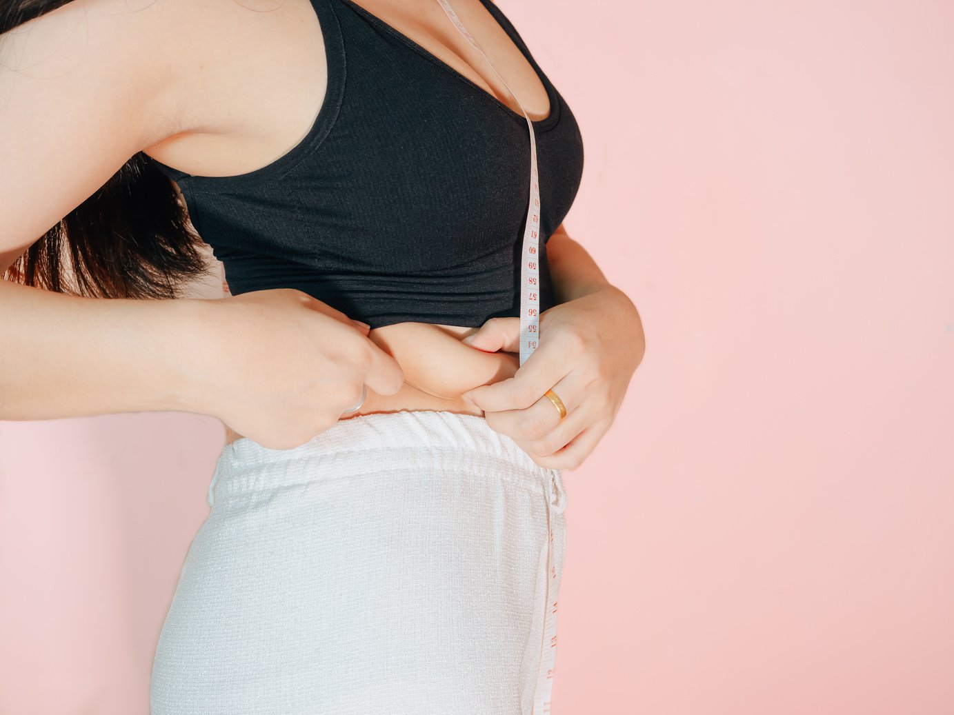 Lose belly fat concept from close up woman in sportswear with hand holding her own belly fat and cellulite.